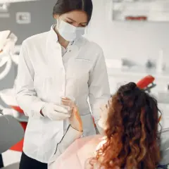 Dentystka w masce podaje wodę pacjentce. Bezpieczne leczenie kanałowe w ciąży jest możliwe.