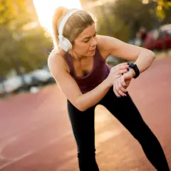Kobieta w słuchawkach sprawdza czas na zegarku, przygotowując się do biegu na 10 km. Czas amatora jest ważny, ale liczy się też radość z wysiłku.