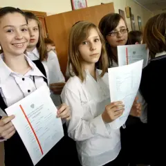 Uczennice z dumą trzymają świadectwa ukończenia szkoły. Na jednym z nich widoczny jest czerwony pasek średnia.