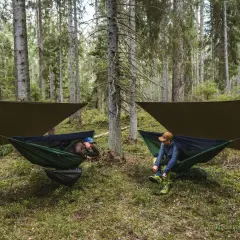 Dwóch mężczyzn odpoczywa w hamakach rozpiętych między drzewami w lesie. Pokazują, jak zawiesić hamak, by cieszyć się naturą.