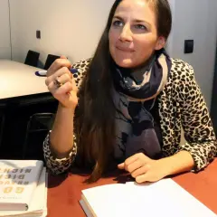 Esther Maria Magnis hält einen Stift und blickt nachdenklich. Auf dem Tisch liegt ihr Buch "Gott braucht dich nicht".
