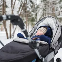 Słodki niemowlak śpi w wózku podczas zimowego spaceru. Otulony ciepłym kombinezonem i czapką, odpoczywa wśród zaśnieżonych drzew.