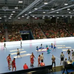 Handballspiel in der Gummersbach Schwalbe Arena. Zuschauer füllen die Ränge, Spieler auf dem Feld, eine Maskottchen-Figur und Cheerleader sind zu sehen.