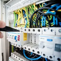 Elektryk naprawia skrzynkę z bezpiecznikami, by rozwiązać problem z brakiem prądu w jednym pokoju.