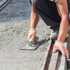 Pracownik w rękawiczkach wygładza świeży beton kielnią. To kluczowy etap, jak zrobić suchy beton, by był równy i trwały.