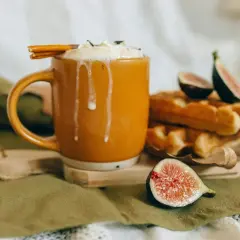 En varm kopp chai latte med vispad grädde och kanelstång, bredvid nybakade våfflor och färska fikon. Perfekt för ett mysigt chai latte recept.