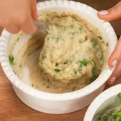 En hand rör i en skål med krämiga refried beans och färska örter.