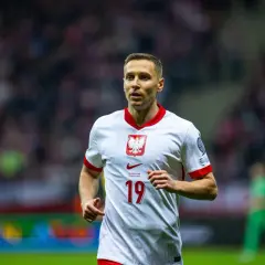 Frankowski piłkarz w białej koszulce z orłem na piersi, numer 19. Biegnie po boisku, skupiony na grze.