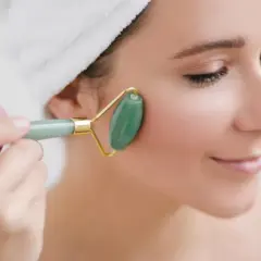 En kvinna med handduk i håret använder en grön jade roller för ansiktet.