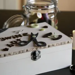 Un costurero pequeño decorado con letras, tijeras de fieltro y botones. Un tarro lleno de hilos y tijeras completan la escena.
