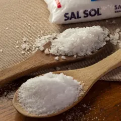 Dos cucharas de madera muestran cómo se obtiene la sal: una con sal marina gruesa y otra con sal fina, junto a un paquete de Sal Sol.
