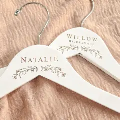 Perchas blancas personalizadas con nombres "Natalie" y "Willow Bridesmaid", adornadas con delicados motivos florales.