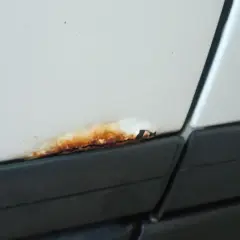 Małe ogniska rdzy na białym samochodzie, tuż nad czarną listwą. Czas na ich usunięcie!