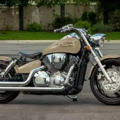 Beżowy motocykl Honda VTX 1300 z chromowanymi elementami i napisem "Blue Collar Bobbers" na baku, zaparkowany na ulicy.