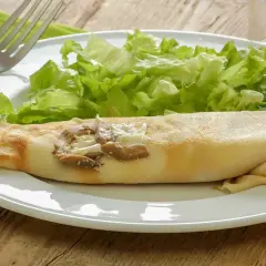 Une ficelle picarde garnie de champignons et de fromage, accompagnée d'une salade verte croquante sur une assiette blanche.