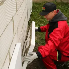 Pracownik w czerwonym stroju montuje płyty styropianu na ścianie z bloczków. To kluczowy etap prac, który decyduje o tym, ile styropianu na strop betonowy będzie potrzebne.