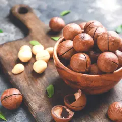 Noci macadamia in una ciotola di legno, con alcune sparse sul tagliere. Scopri i noci macadamia benefici per la tua salute.