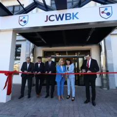 Otwarcie placówki: ludzie przecinają czerwoną wstęgę przed budynkiem z logo JCWBK.