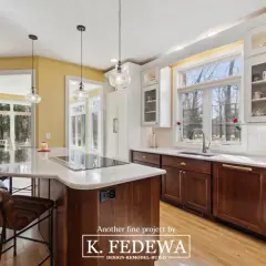 A bright, airy kitchen with natural wood cabinets and a large island. Sunlight streams through large windows, illuminating the warm tones of the wood.