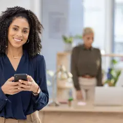 Frau mit Handy lächelt. Sie informiert sich über die **Fernstudium Voraussetzungen** für ihre Karriere.