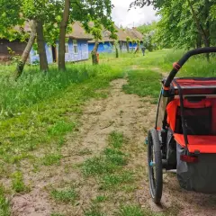 Wózek dziecięcy na tle tradycyjnych, niebieskich chat z krytymi strzechą dachami. Idealne miejsce na wycieczkę, odkrywanie ciekawych miejsc 200 km od Łodzi.