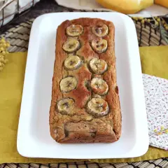 Delizioso banana bread light, decorato con fette di banana, su un piatto bianco, con fiori di mimosa sullo sfondo.