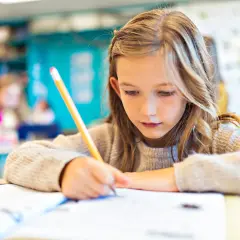 Dziewczynka skupiona na nauce, pisze w zeszycie. Czy jest obowiązek nauki do 18 roku życia? Tak, edukacja jest ważna!
