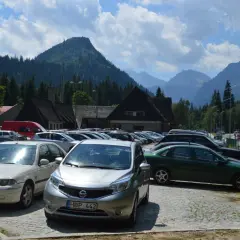 Na łysa polana parking, pełen samochodów, z górami w tle.