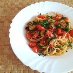 Un piatto di spaghetti con le cozze e pomodorini freschi, guarnito con prezzemolo tritato, pronto per essere gustato.