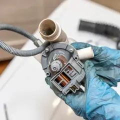 Naprawa pompy pralki, która nie odpompowuje wody. Widoczny element z wężem i złączem elektrycznym.