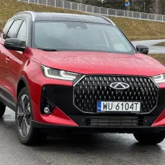 Czerwone auto Chery z czarnym grillem i felgami stoi na mokrej drodze.