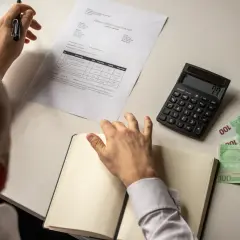 Mężczyzna analizuje fakturę, kalkulator i pieniądze. Zastanawia się, czy przegrany pokrywa koszty adwokata.