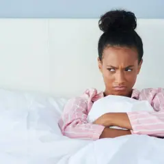 Chica enfadada en la cama, pensando en excusas para no quedar.