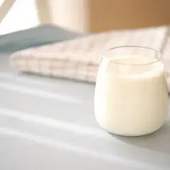 Szklanka mleka 2% na jasnym tle z tkaniną w kratkę.