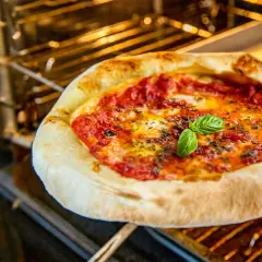 Frisch gebackene pizza vom blech mit geschmolzenem Käse und Basilikum im Ofen.