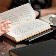 Konwergencja tradycji i technologii: ręka czyta książkę, która spoczywa na tablecie. Obok filiżanka kawy.