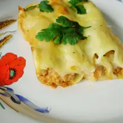 Pyszne cannelloni z mięsem mielonym, zapieczone pod serem i udekorowane natką pietruszki. Danie podane na talerzu z motywem maków i kłosów.