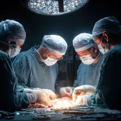 Zespół chirurgów w maseczkach i czepkach skupiony na skomplikowanej operacji pod jasnym światłem lampy.