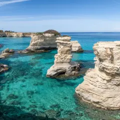 Klippformationer reser sig ur det turkosa vattnet vid Salento, Italien. En kajakpaddlare njuter av den vackra kusten.