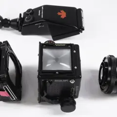 A Mamiya RZ67 camera body, film back, prism finder, and 110mm lens are laid out on a white surface.