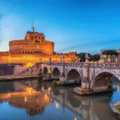 Le Castel Sant'Angelo à Rome, illuminé au crépuscule, se reflète dans le Tibre. Le pont Saint-Ange, orné de statues, mène à cette ancienne forteresse.