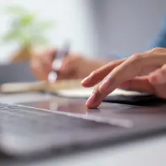 Dłoń na touchpadzie laptopa, obok notatnik. Może to być przygotowanie do złożenia wypowiedzenia OC.