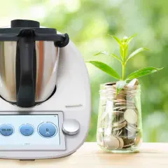 Thermomix i słoik z monetami, symbolizujące oszczędność energii. Dowiedz się, ile prądu pobiera Thermomix, by gotować ekonomicznie.