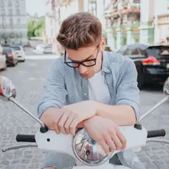 Młody mężczyzna na skuterze, zamyślony. Pomyśl o ubezpieczeniu motoroweru, by podróżować bez obaw.