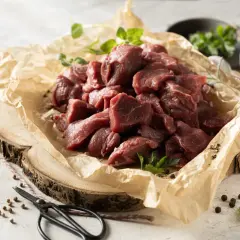 Pokrojone w kostkę mięso dzika, gotowe na aromatyczny gulasz z dzika. Obok gałązki ziół i przyprawy.
