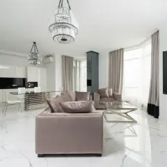 Soggiorno moderno con divani beige, tavolo da caffè in vetro e pavimento in **gres porcellanato cos'è** effetto marmo. Cucina bianca a vista con isola.