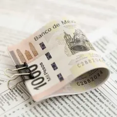 Złożony banknot 100 pesos, przytrzymany spinaczem, leży na dokumentach podatkowych. To pokazuje, co to jest lokata bankowa – sposób na bezpieczne przechowywanie pieniędzy.