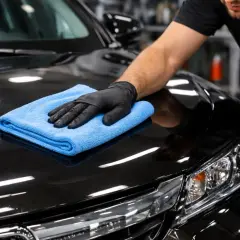Rękawiczka z mikrofibry rozprowadza wosk po czarnej masce auta, nadając jej połysk. Pokazano, jak nakładać wosk na auto.