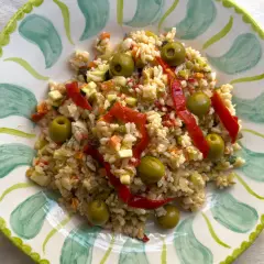 Deliciosa ensalada de arroz con pimientos rojos, aceitunas verdes y verduras picadas, servida en un plato decorado.