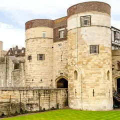 Kamienne wieże Tower of London, pełne ciekawostek, z kratami w oknach i zielonym trawnikiem.
